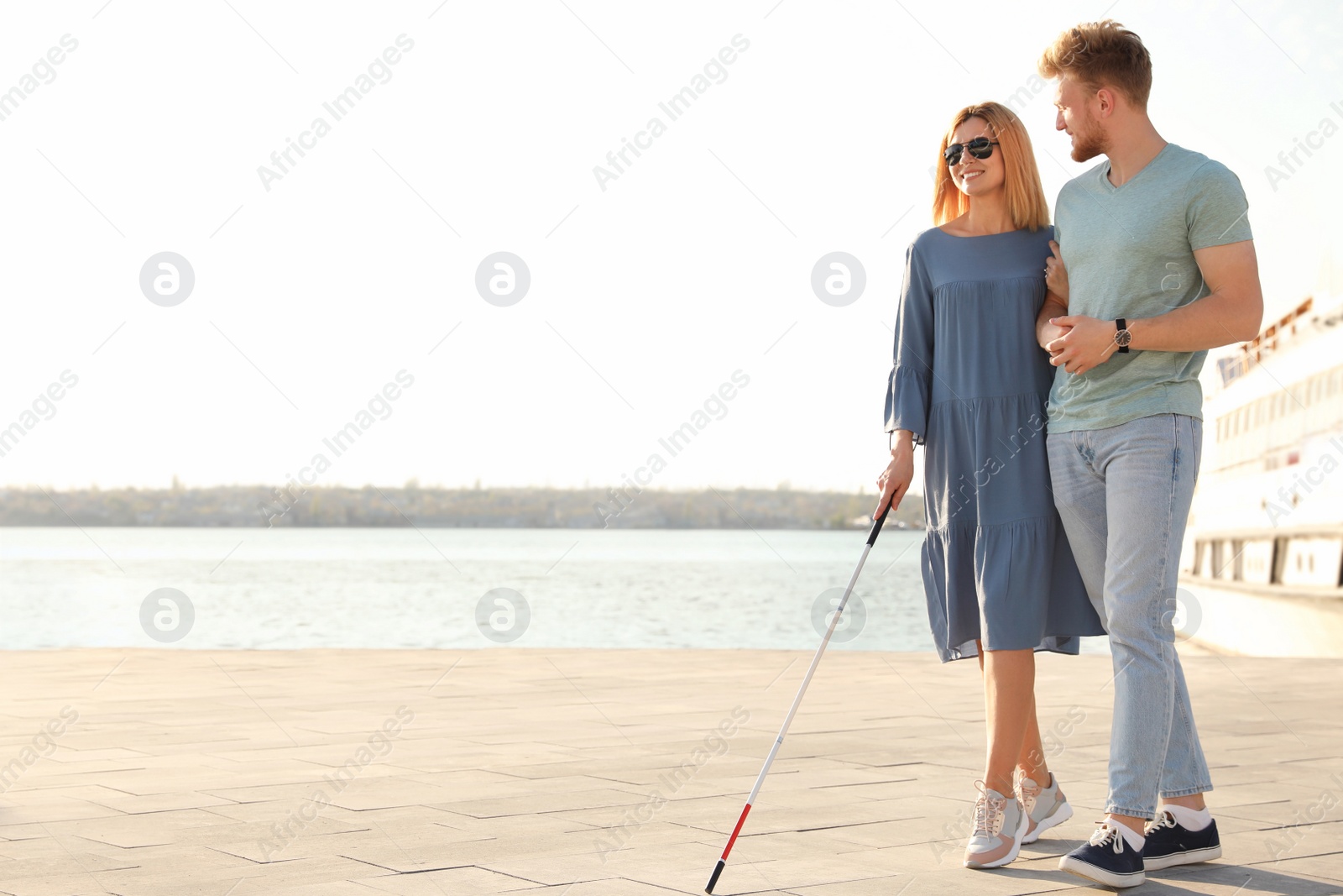 Photo of Young man helping blind person with long cane in city. Space for text