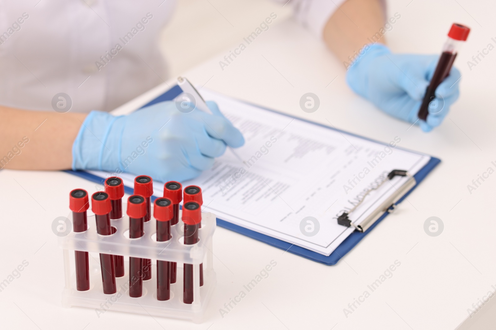 Photo of Doctor with samples of blood in test tubes at white table, closeup