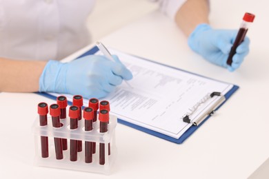 Doctor with samples of blood in test tubes at white table, closeup