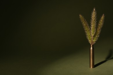 Photo of Bullet cartridge case and green foxtails on color background, space for text