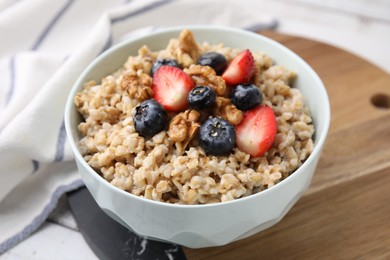 Photo of Tasty oatmeal with strawberries, blueberries and walnuts in bowl on white wooden table, closeup