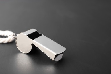 Referee whistle with cord on black textured table, closeup. Space for text