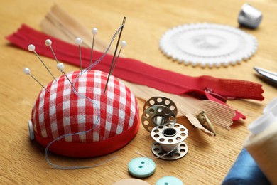 Pincushion and sewing tools on wooden table, closeup