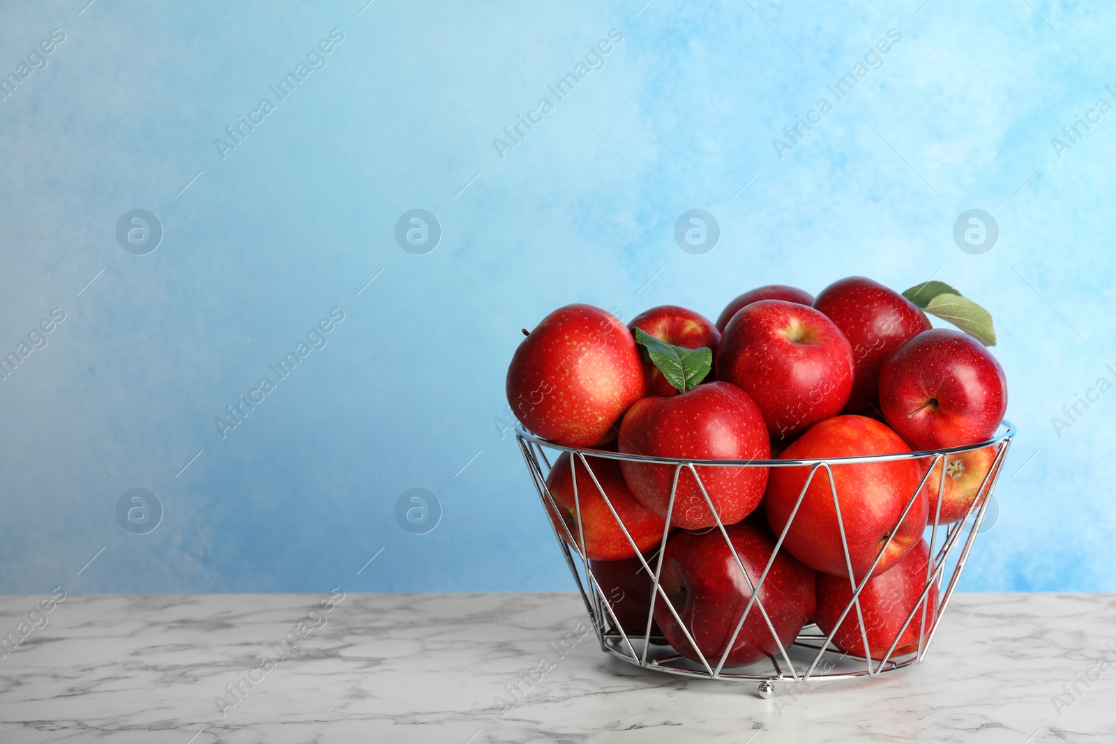 Photo of Juicy red apples in metal basket on table. Space for text