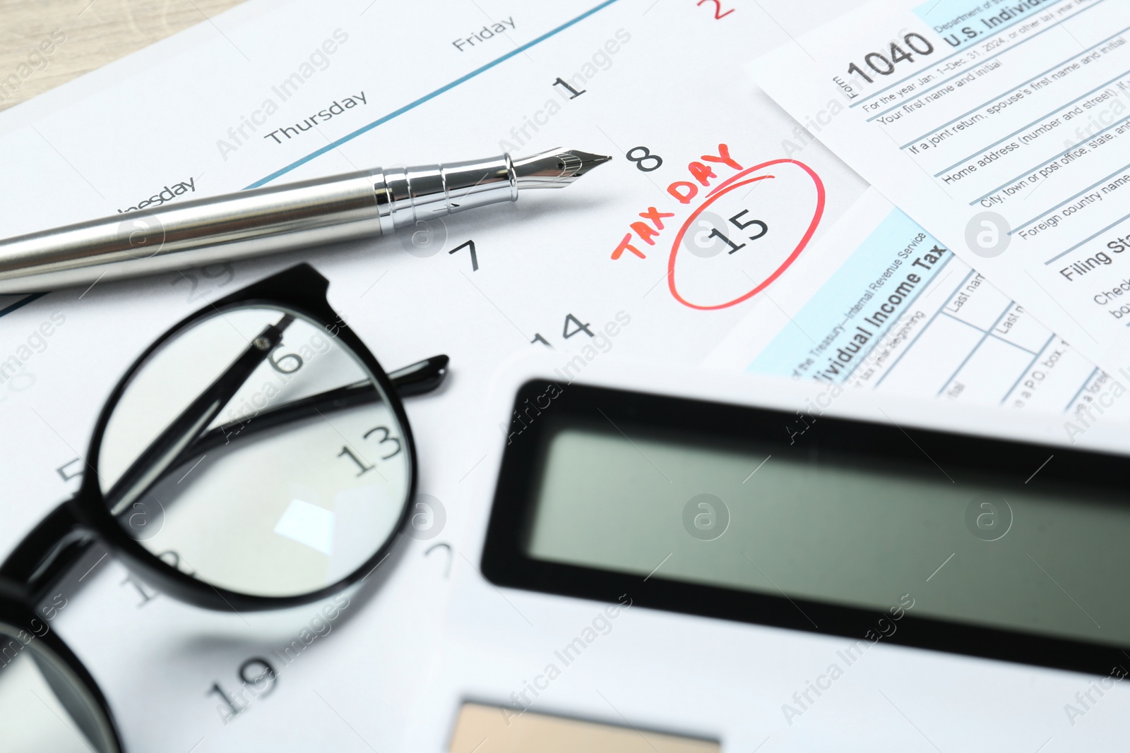 Photo of Tax day. Calendar with date reminder, documents, pen, calculator and glasses on table