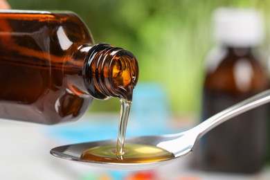 Photo of Pouring syrup from bottle into spoon on blurred background, closeup. Cold medicine