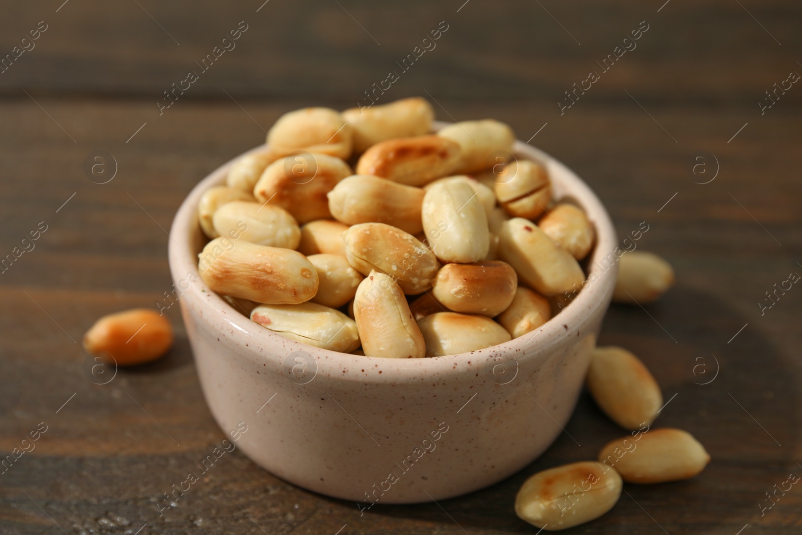 Photo of Roasted peanuts in bowl on wooden table, closeup