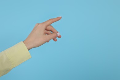 Photo of Woman pointing at something against light blue background, closeup on hand. Space for text