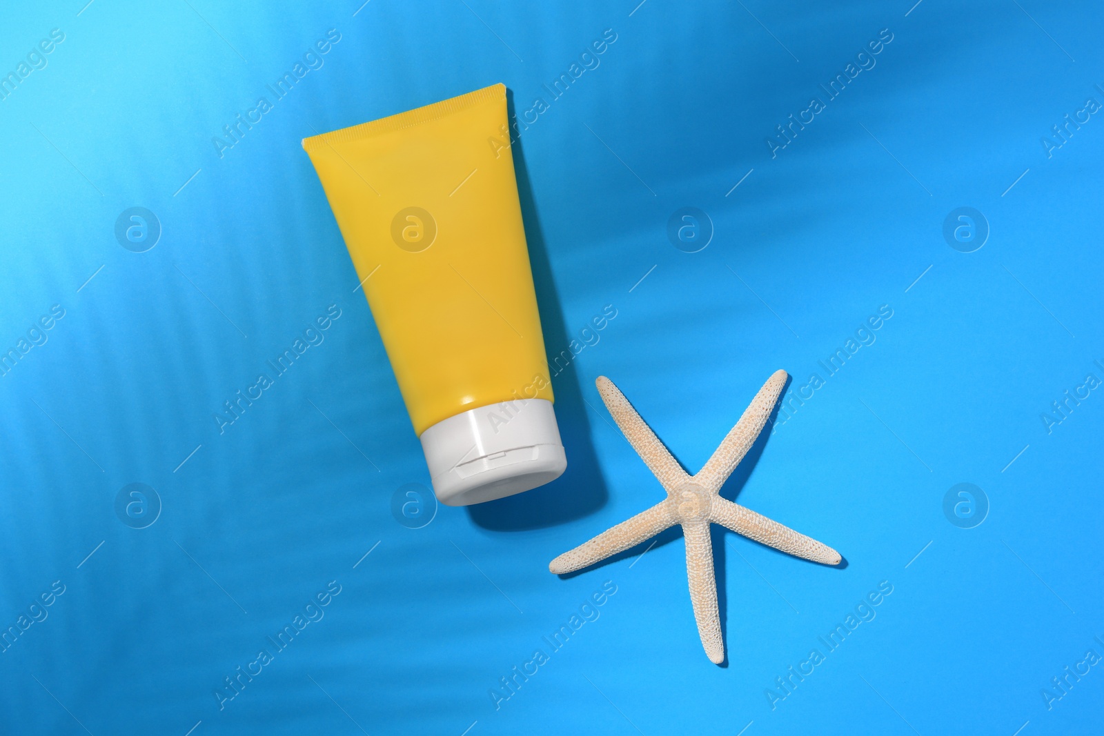 Photo of Sunscreen and starfish on light blue background, flat lay. Sun protection care