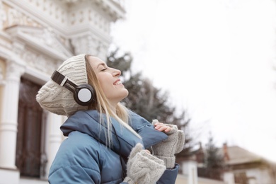 Photo of Young woman with headphones listening to music outdoors. Space for text