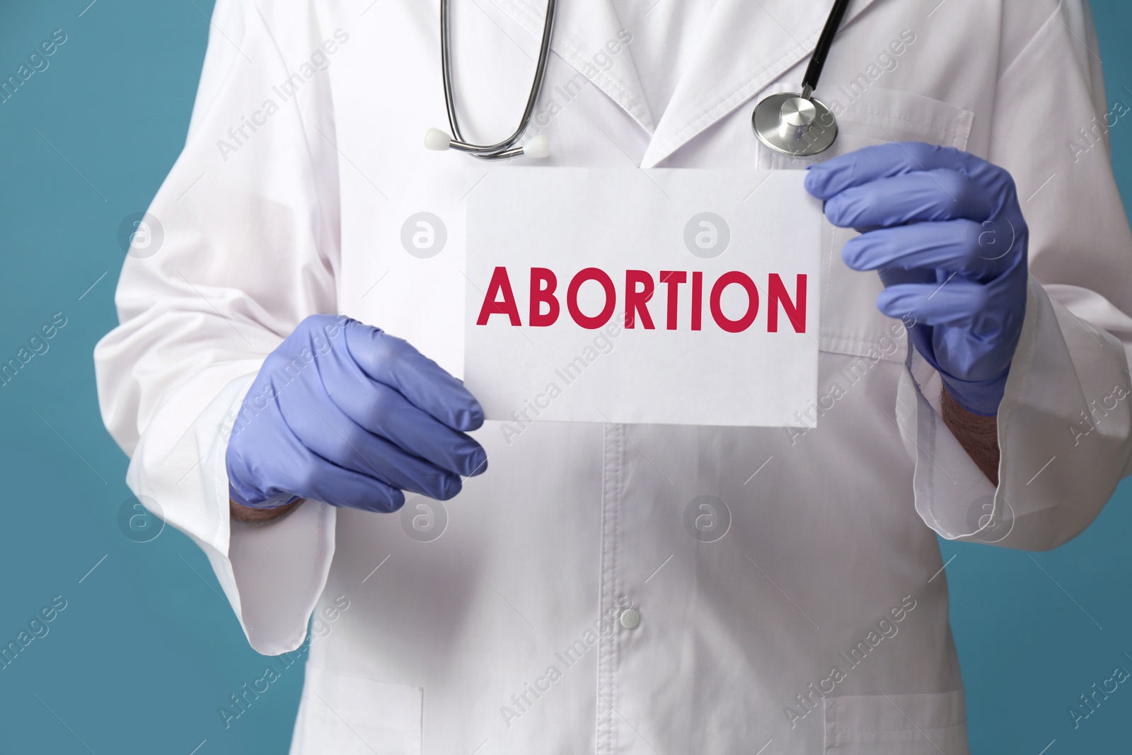 Image of Doctor holding paper card with word Abortion on light blue background, closeup