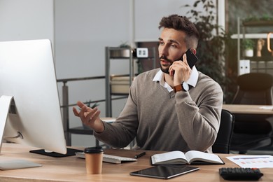 Photo of Man talking on phone while working at table in office
