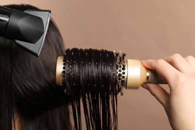 Photo of Hairdresser blow drying client's hair on light brown background, closeup