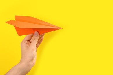 Woman holding paper plane on yellow background, closeup. Space for text