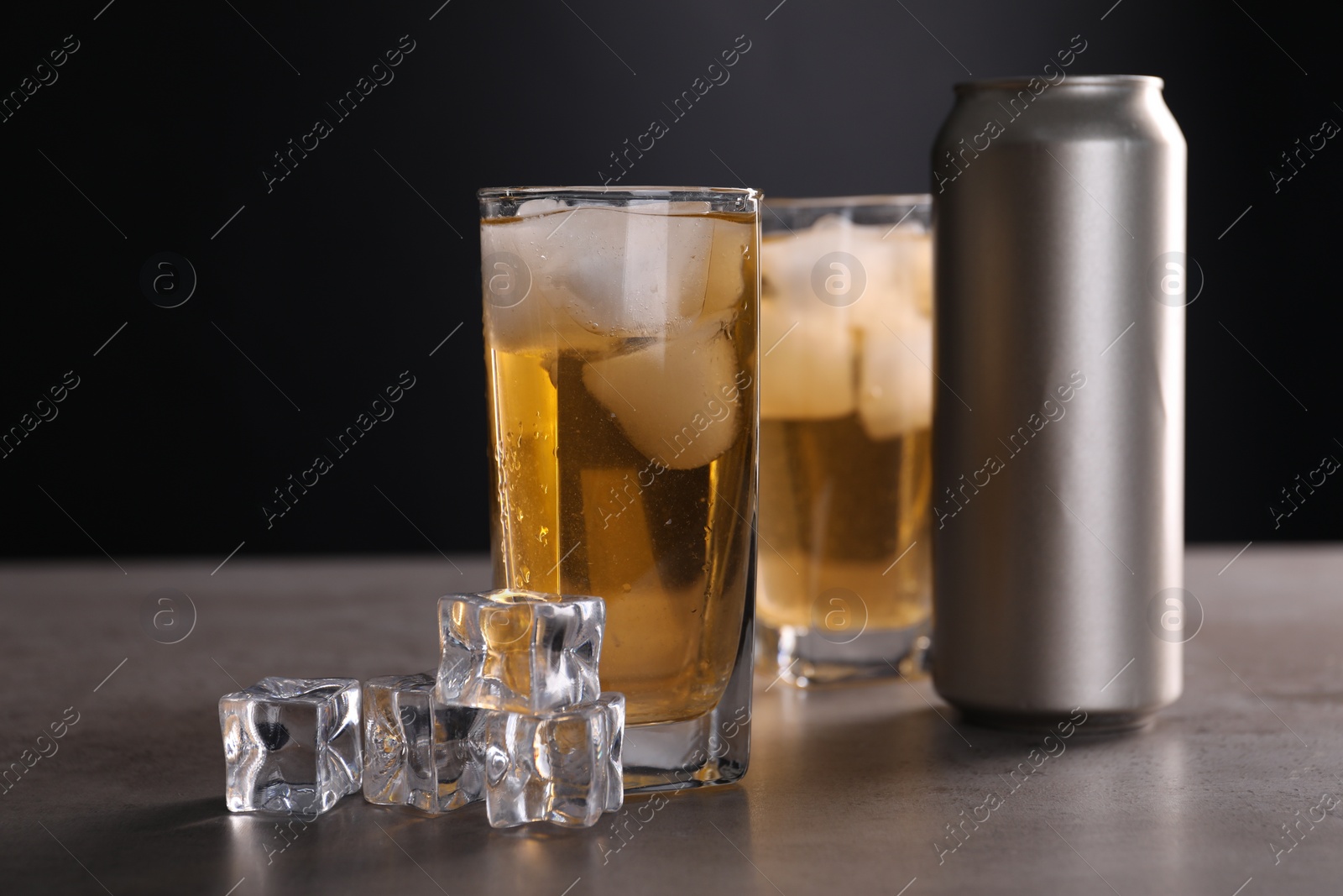 Photo of Energy drink in glasses, aluminium can and ice cubes on grey table