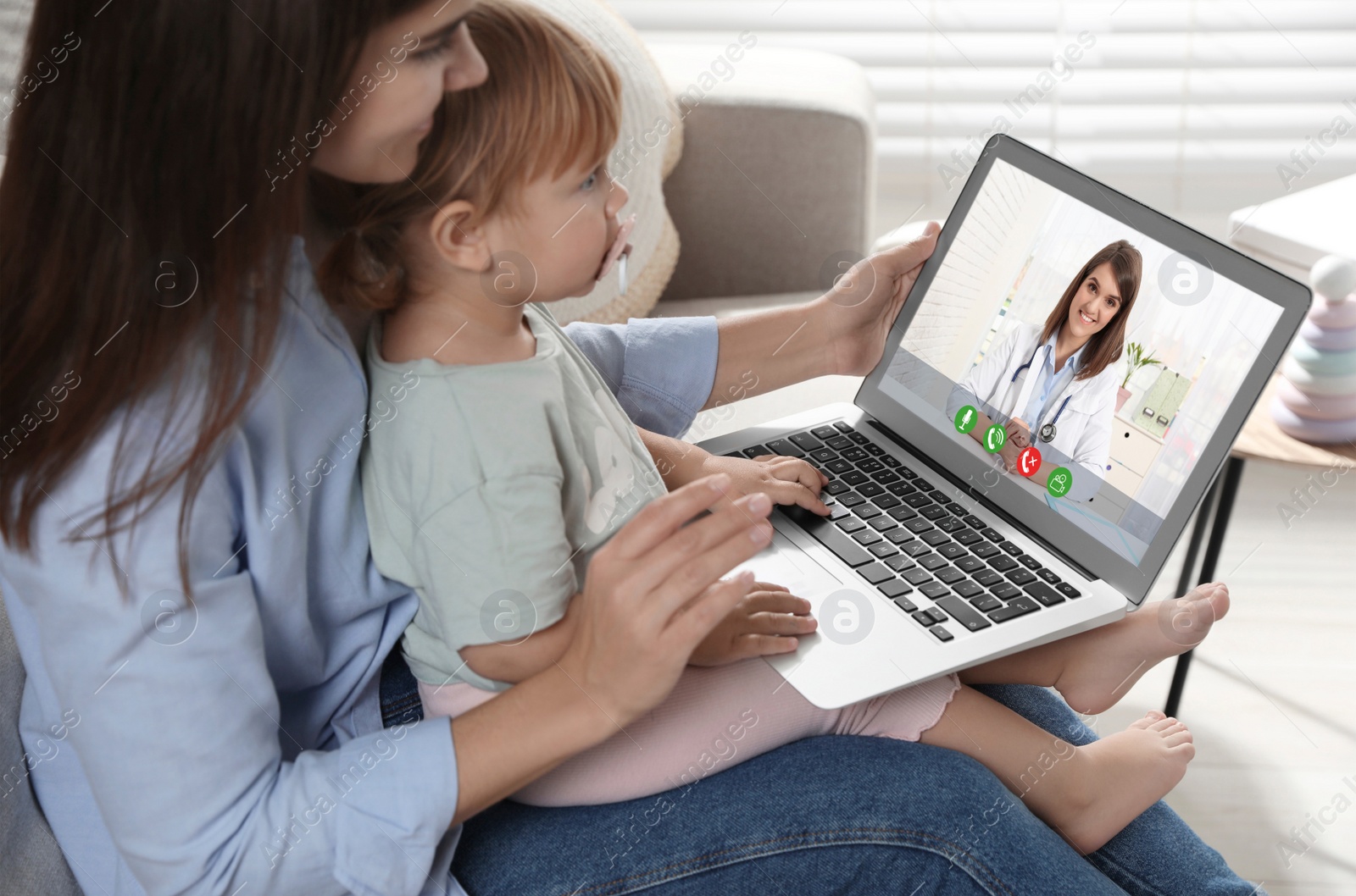 Image of Mother and daughter having online consultation with pediatrician via laptop on sofa at home