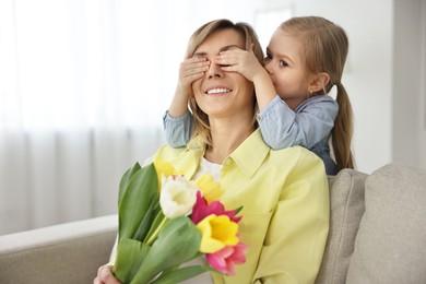 Photo of Little girl surprising her mom with bouquet of tulips at home. Happy Mother`s Day