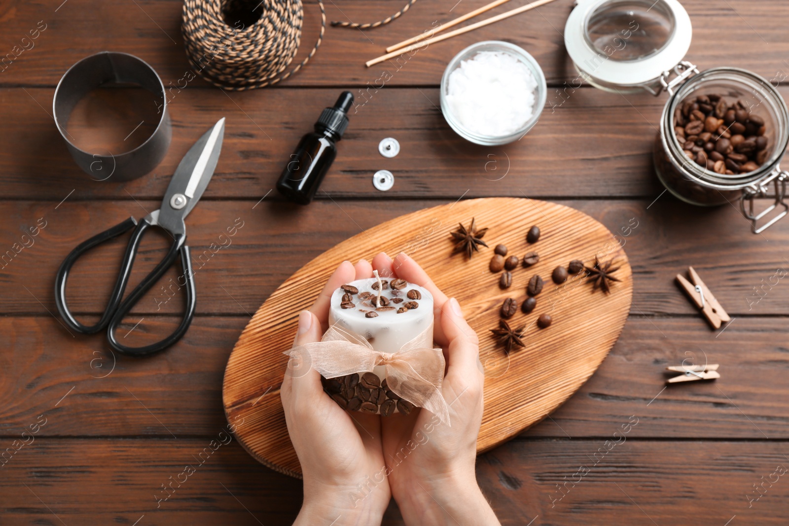 Photo of Woman holding coffee candle at wooden table, top view