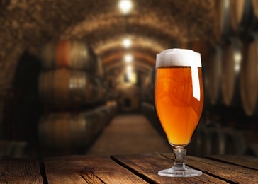Image of Glass of tasty beer on wooden table in cellar with large barrels, space for text