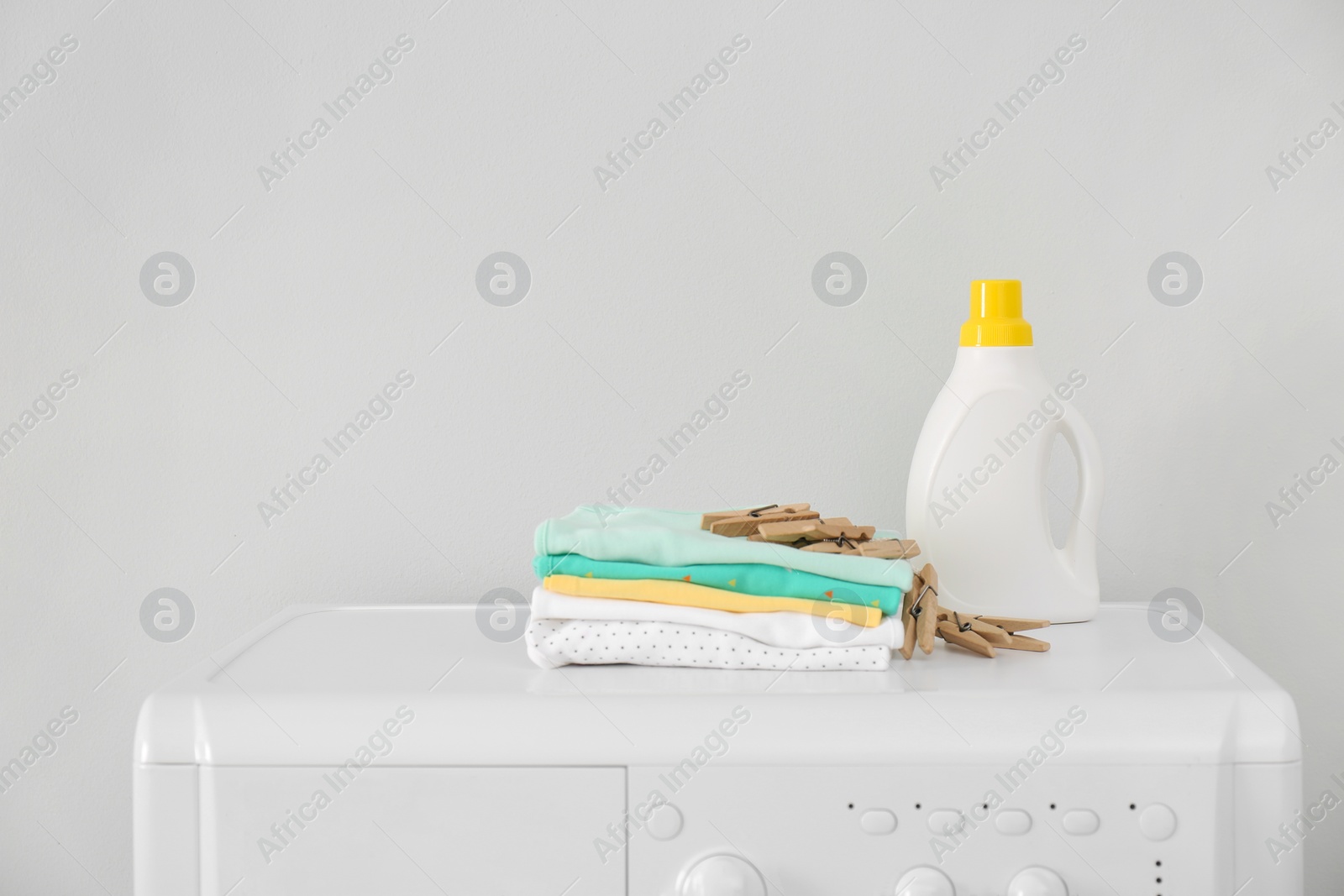 Photo of Bottle of detergent and children's clothes on washing machine