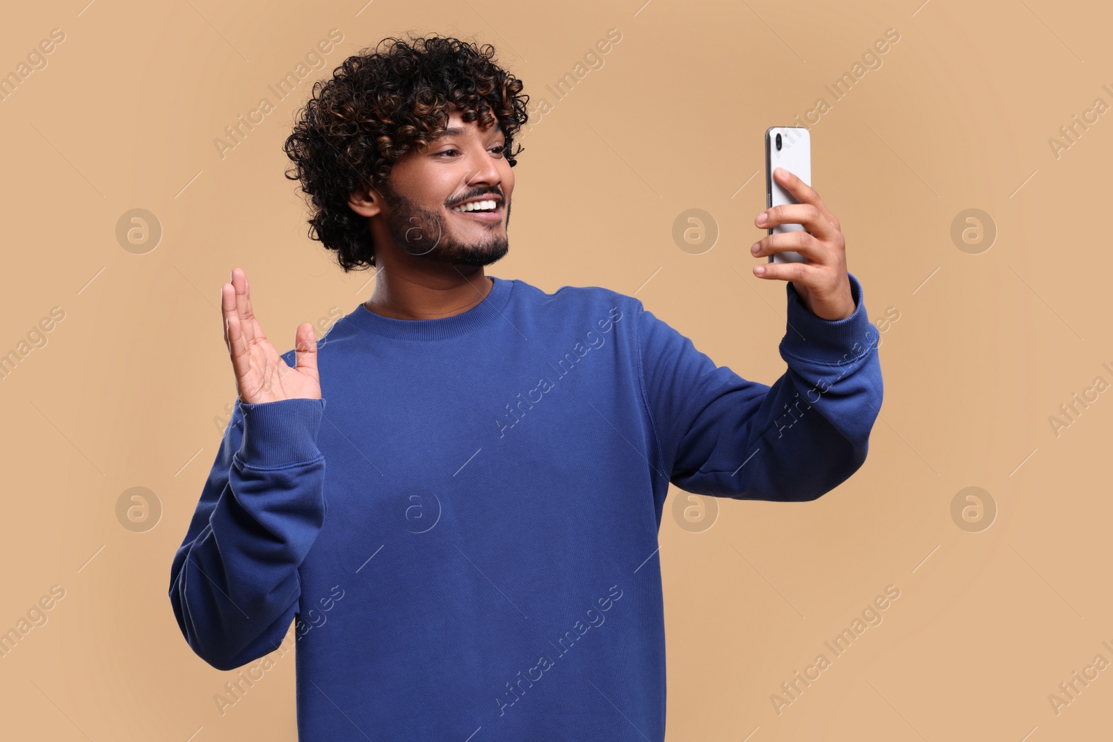 Photo of Handsome smiling man having video call via smartphone on beige background