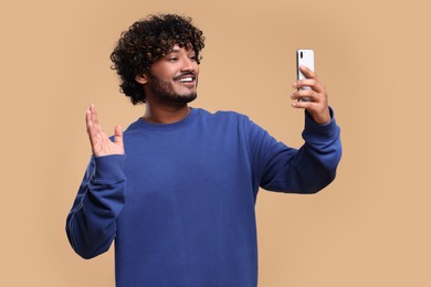 Photo of Handsome smiling man having video call via smartphone on beige background