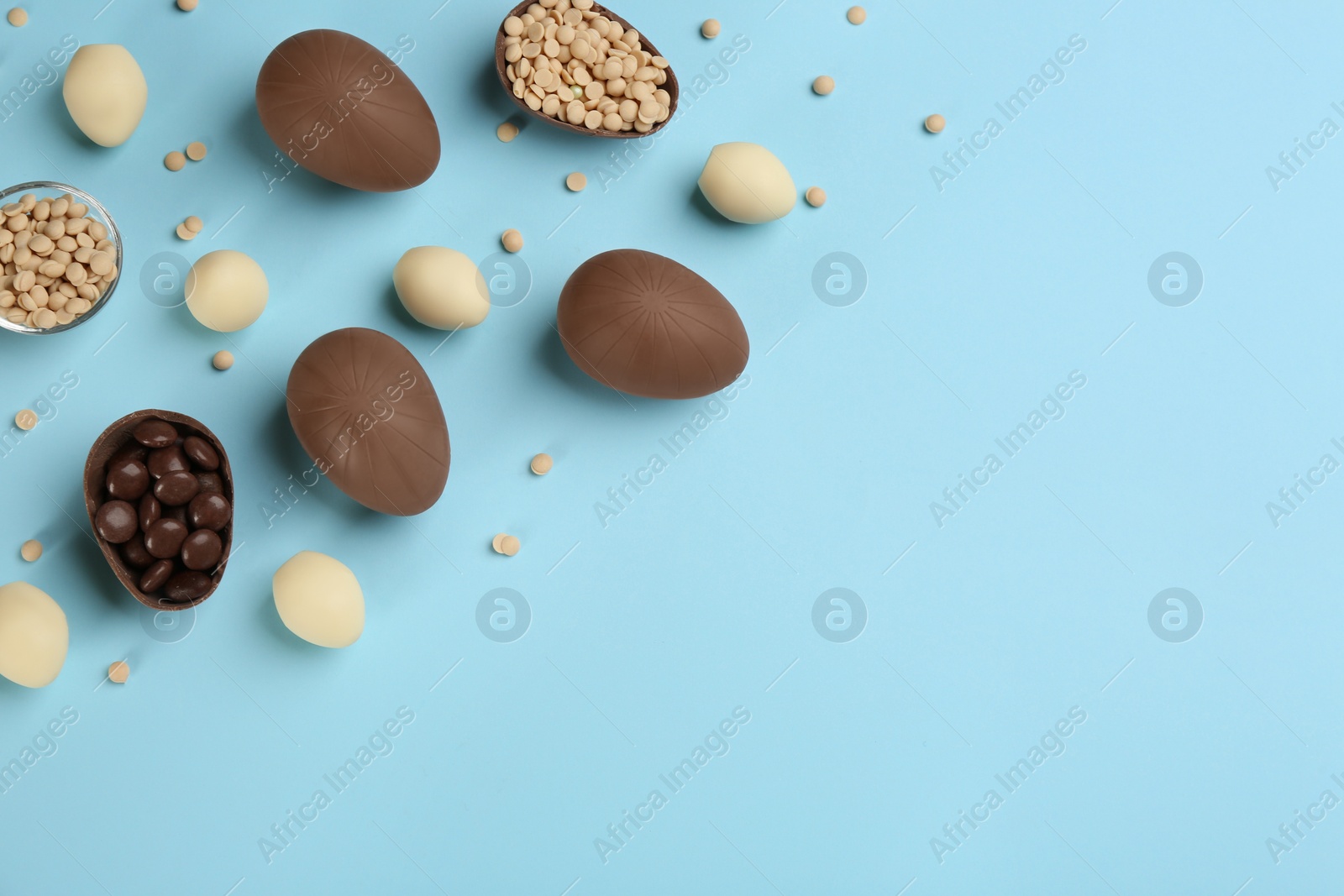 Photo of Sweet chocolate eggs and candies on light blue background, flat lay. Space for text