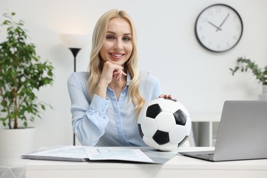 Happy woman with soccer ball at table in office