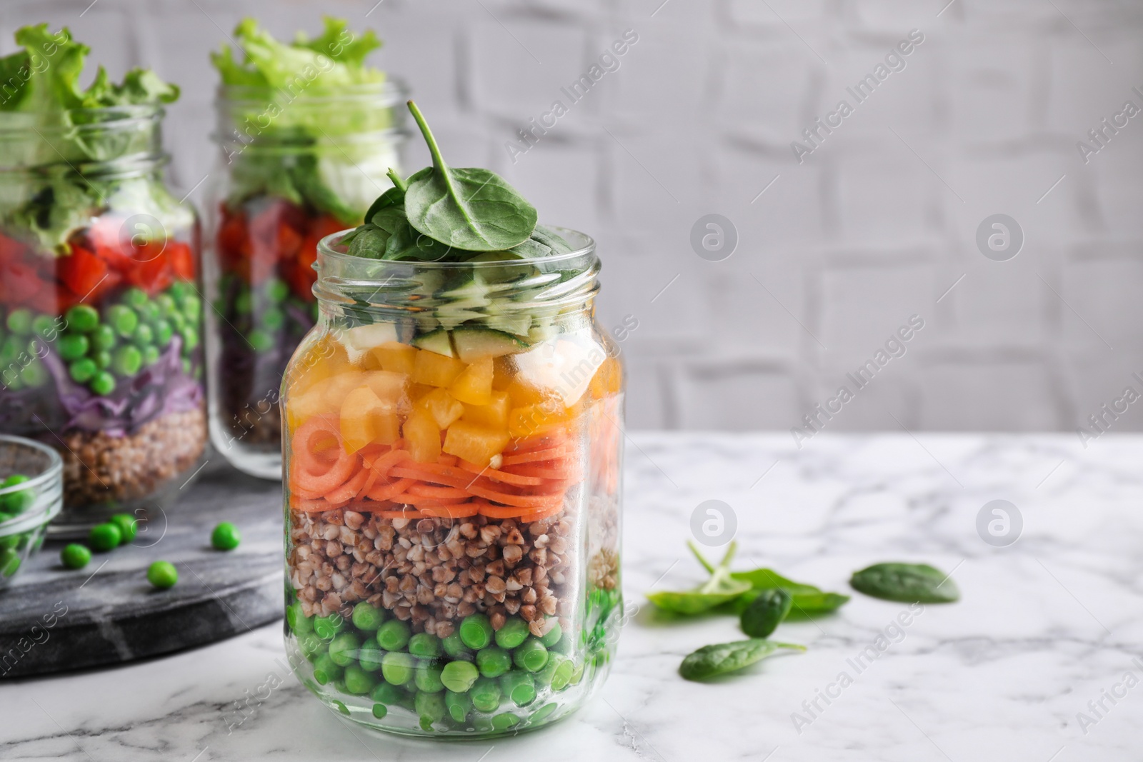 Photo of Healthy salads in glass jars on marble table. Space for text