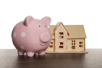 Photo of Piggy bank and house model on wooden table against white background. Saving money concept