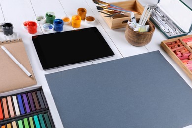 Photo of Blank sheet of paper, colorful chalk pastels, tablet and other drawing tools on white wooden table. Modern artist's workplace