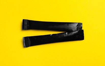 Photo of Black sticks of sugar on yellow background, flat lay