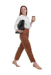 Beautiful businesswoman with briefcase and paper cup of coffee walking on white background