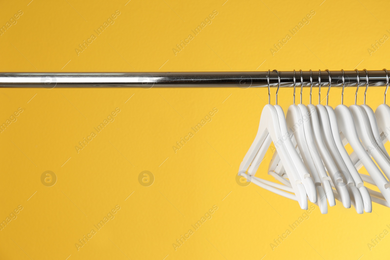 Photo of Metal rack with clothes hangers on color background, space for text