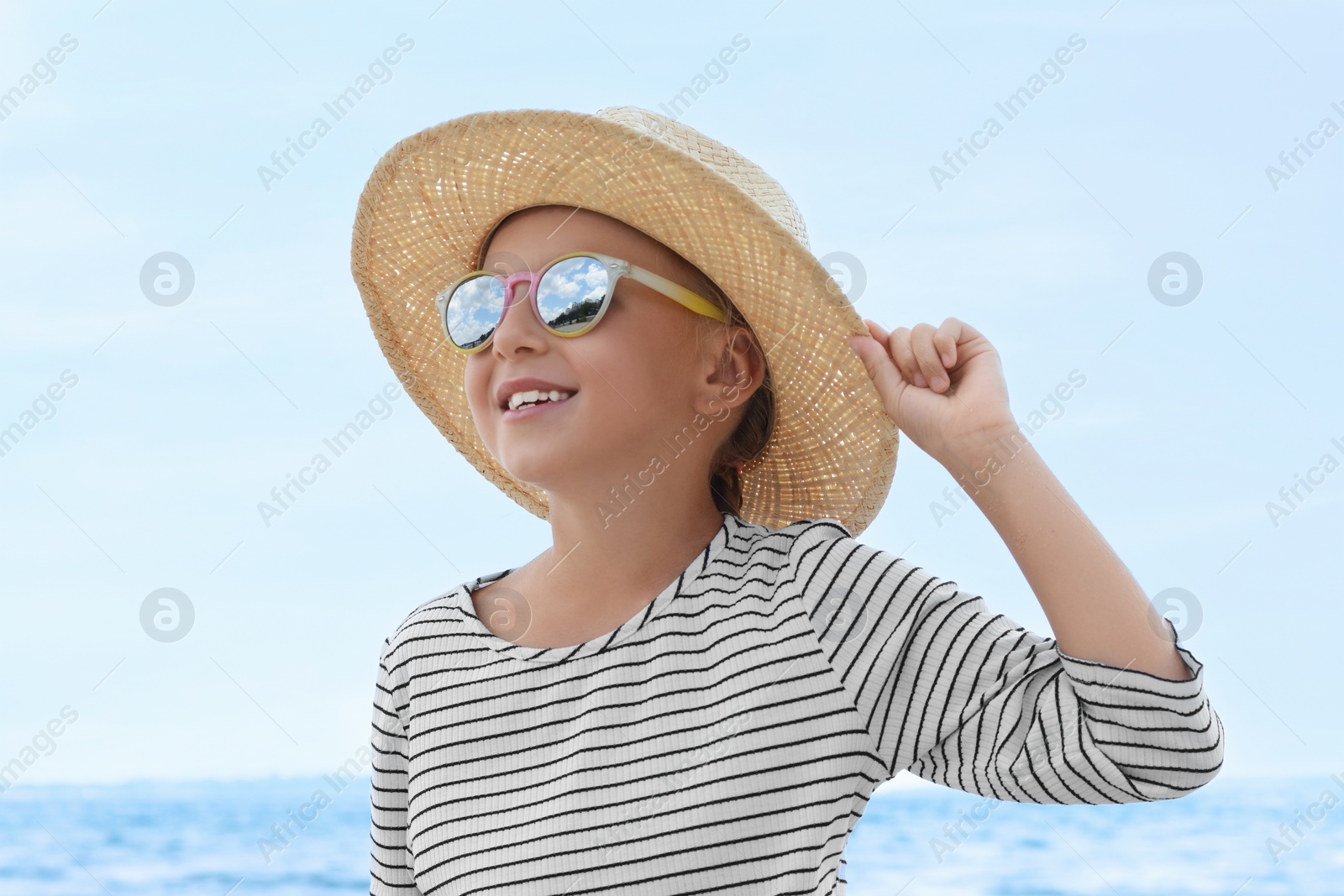 Photo of Little girl wearing sunglasses and hat at beach on sunny day