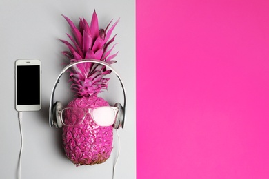 Photo of Pineapple with headphones, glasses and smartphone on color background, top view with space for text