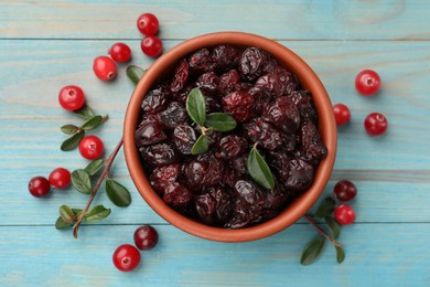 Photo of Tasty dried cranberries in bowl, fresh ones and leaves on light blue wooden table, top view