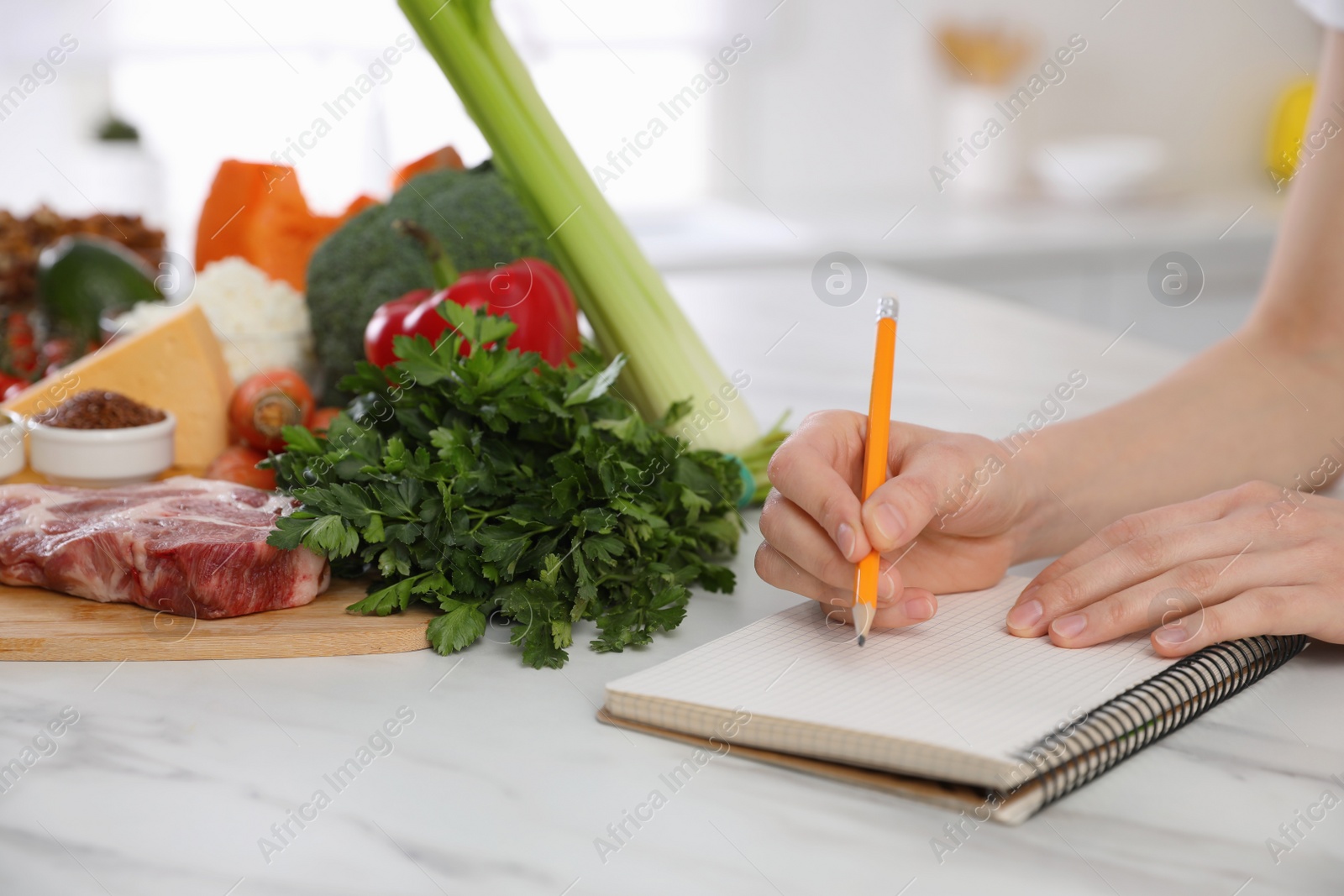 Photo of Woman with notebook and healthy food at white table, closeup. Keto diet