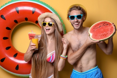Photo of Young couple in beachwear with inflatable ring and watermelon on color background