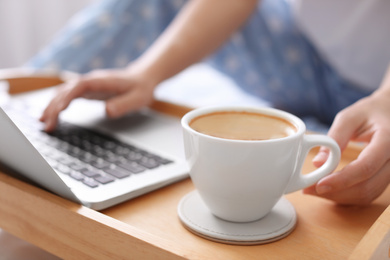 Photo of Woman taking cup of morning coffee while working on laptop indoors, closeup
