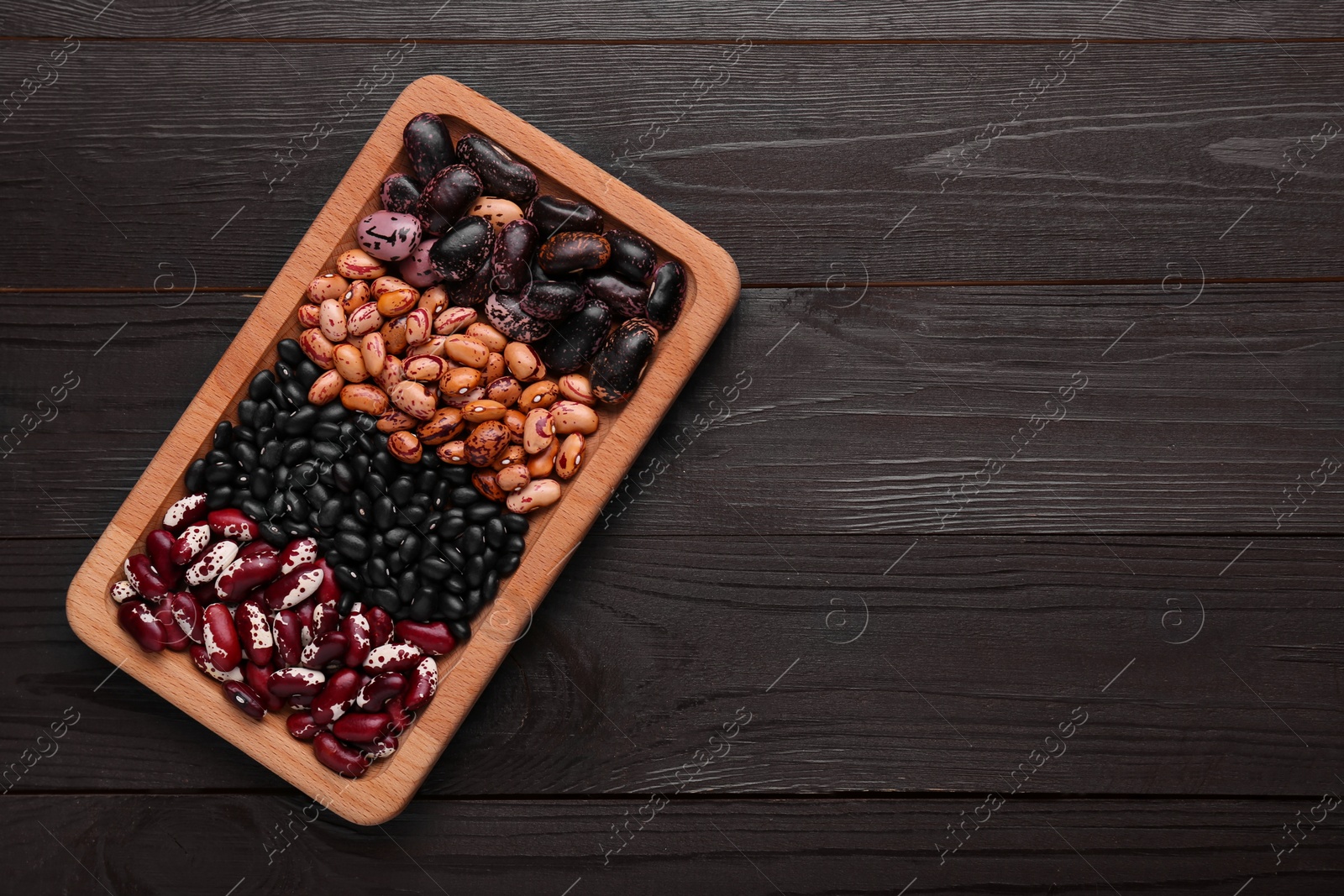 Photo of Plate with different kinds of dry kidney beans on wooden table, top view. Space for text