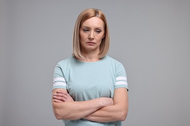 Portrait of sad woman with crossed arms on grey background