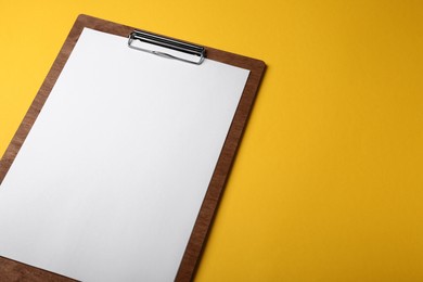 Photo of Wooden clipboard with sheet of blank paper on yellow background. Space for text