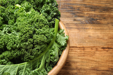 Photo of Fresh kale leaves on wooden table, closeup. Space for text