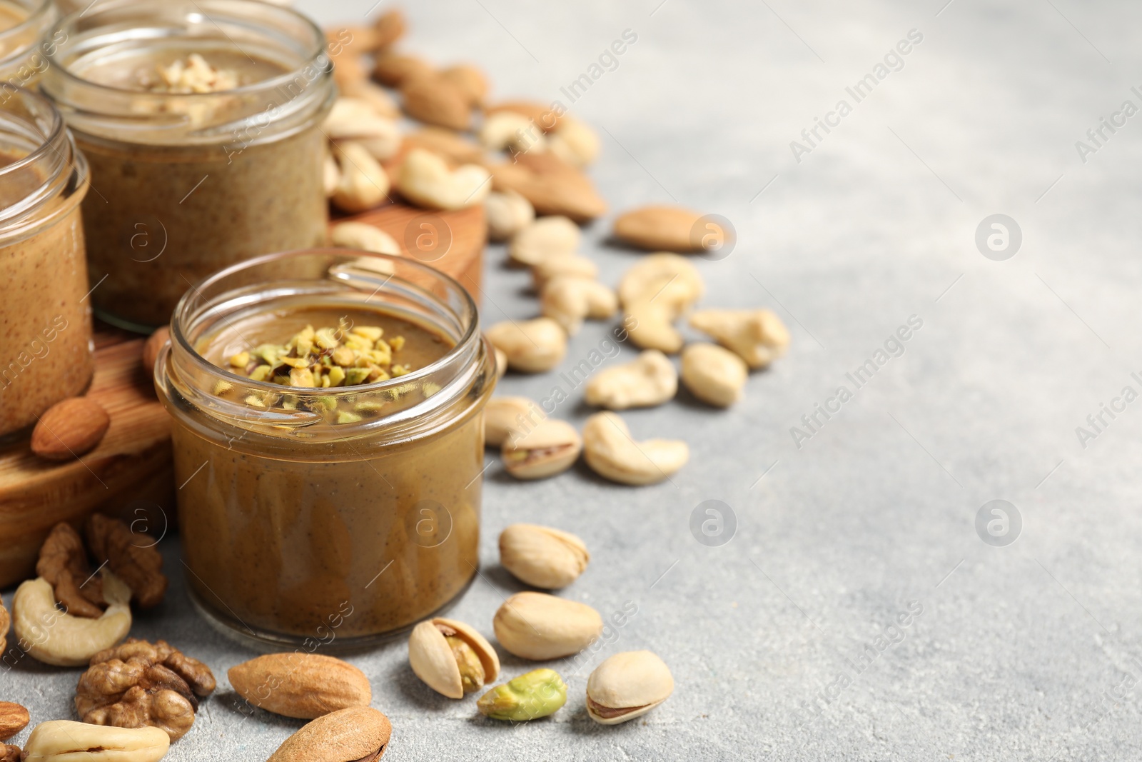 Photo of Tasty nut butters in jars and raw nuts on light grey table, space for text