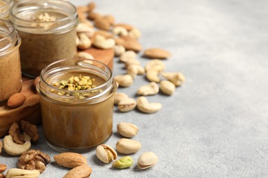 Photo of Tasty nut butters in jars and raw nuts on light grey table, space for text