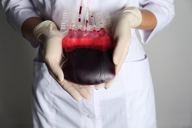 Woman holding blood for transfusion on light grey background, closeup. Donation concept