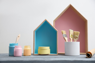 Photo of Brush with paint and wooden houses on grey table