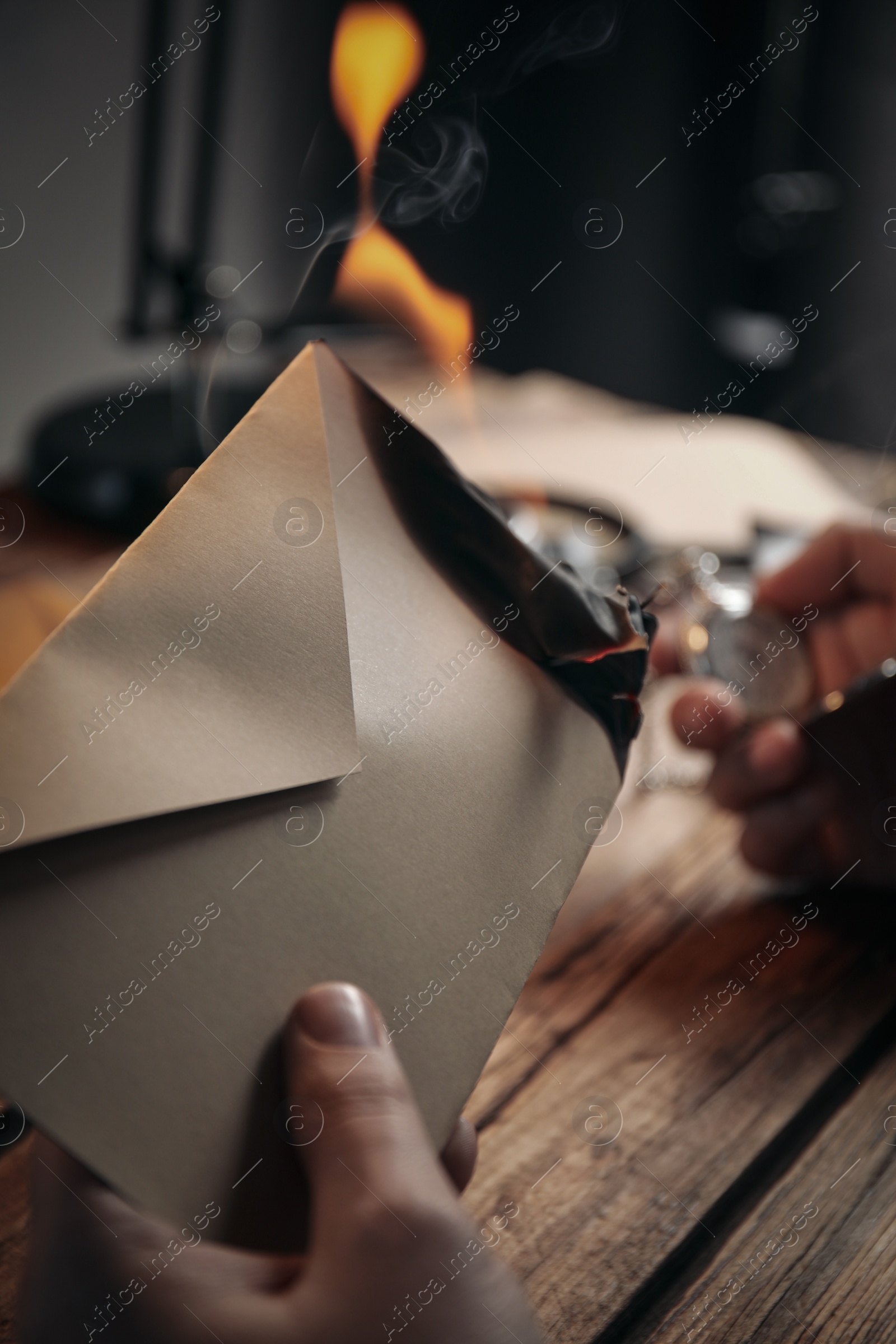 Photo of Detective with burning envelope and pocket watch at wooden table, closeup