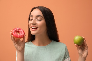 Photo of Woman choosing between apple and doughnut on orange background
